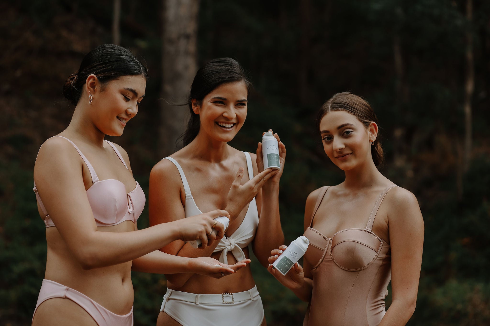 three models holding wild fusion skincare calming day cream, advanced hydration night cream and manuka hydra gel with an Australian forest background