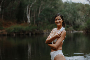 model standing in the river looking away and up to the sky holding a tube of wild fusion skincare glycolic facial polish and scrub